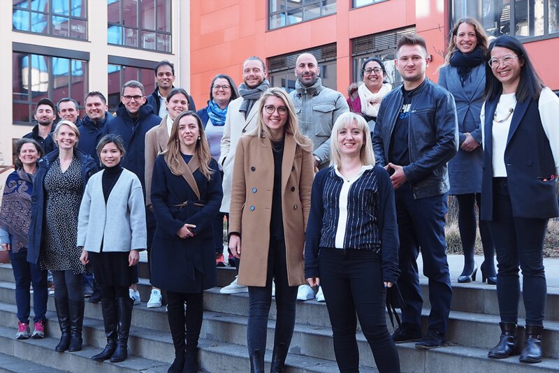 Eine Gruppe von etwa 20 Personen in Mänteln und Jacken posiert auf den Stufen des WHU-Campus in Düsseldorf. 
